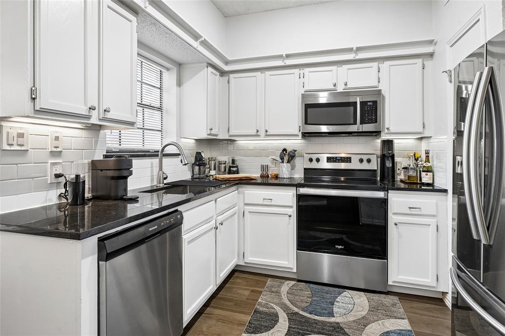 Kitchen featuring white shaker-style cabinetry, dark stone countertops, stainless steel appliances, and a subway tile backsplash