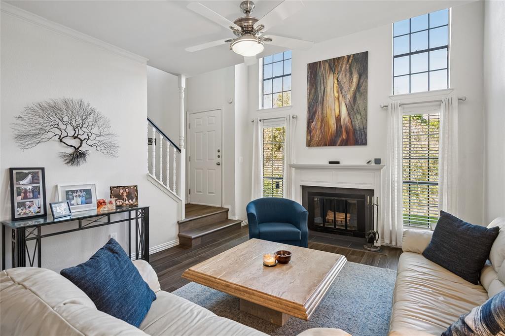 Living area featuring a double-height ceiling, fireplace with a mantel, tall paneled windows, wood-finish flooring, and a ceiling fan