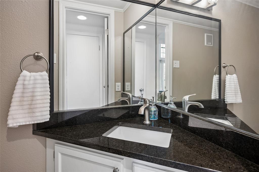 Dark stone countertop featuring an integrated undermount sink, white cabinetry, a large-format mirror with black trim, and a brushed nickel finish faucet