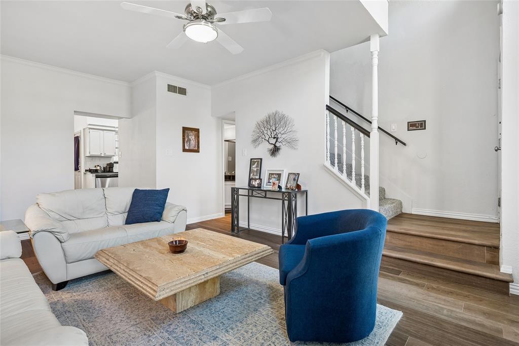 Living area featuring wood-finish flooring, staircase with a white balustrade and wooden handrail, and a ceiling fan with integrated lighting
