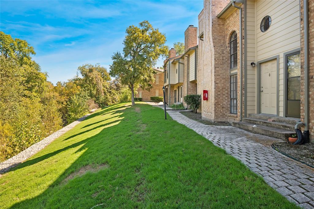 Multi-level exterior featuring brick and siding construction, arched window accents, a paved stone walkway, and an expansive grass lawn with mature trees