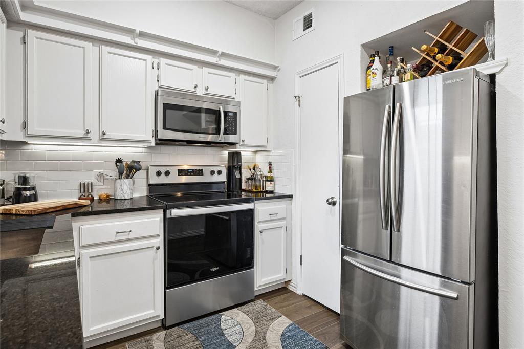 Kitchen featuring white shaker-style cabinetry, dark stone countertops, a white subway tile backsplash, and stainless steel appliances