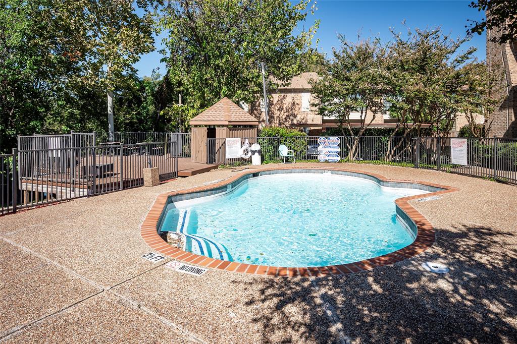 In-ground swimming pool featuring a brick-accented border, aggregate pool decking, an elevated wooden deck, and a wooden gazebo