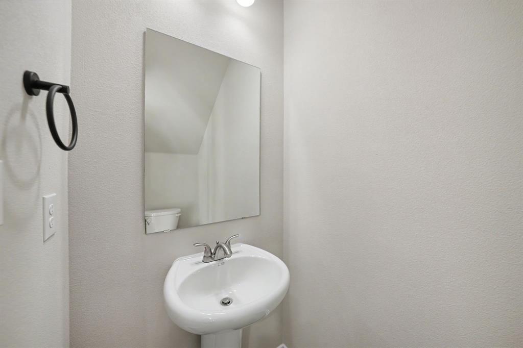 Pedestal sink with a chrome faucet, wall-mounted mirror, and a matte black towel ring