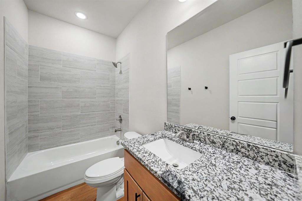 Bathroom featuring a single vanity with stone countertop, integrated sink, wood-finish cabinetry, and a bathtub with tiled surround