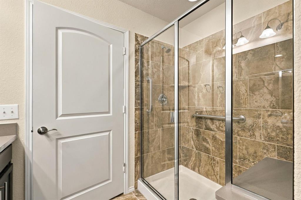 Walk-in shower featuring metallic-finish frame, stone-tile surround, integrated bench seating, and dual wall-mounted grab bars