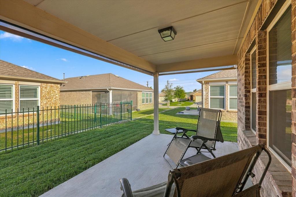 Covered concrete patio featuring a ceiling-mounted light fixture, brick exterior wall, metal fencing, and grass lawn