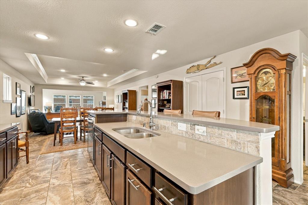 Kitchen featuring dark-finish cabinetry, neutral-toned solid surface countertops, a dual-basin stainless steel undermount sink, stone-tiled backsplash, and recessed lighting