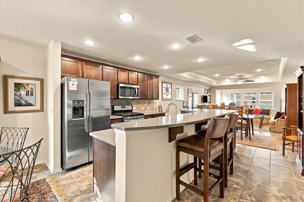 Kitchen featuring dark-finish wood cabinetry, stainless steel appliances, solid surface countertops with an integrated breakfast bar, and stone-tile flooring