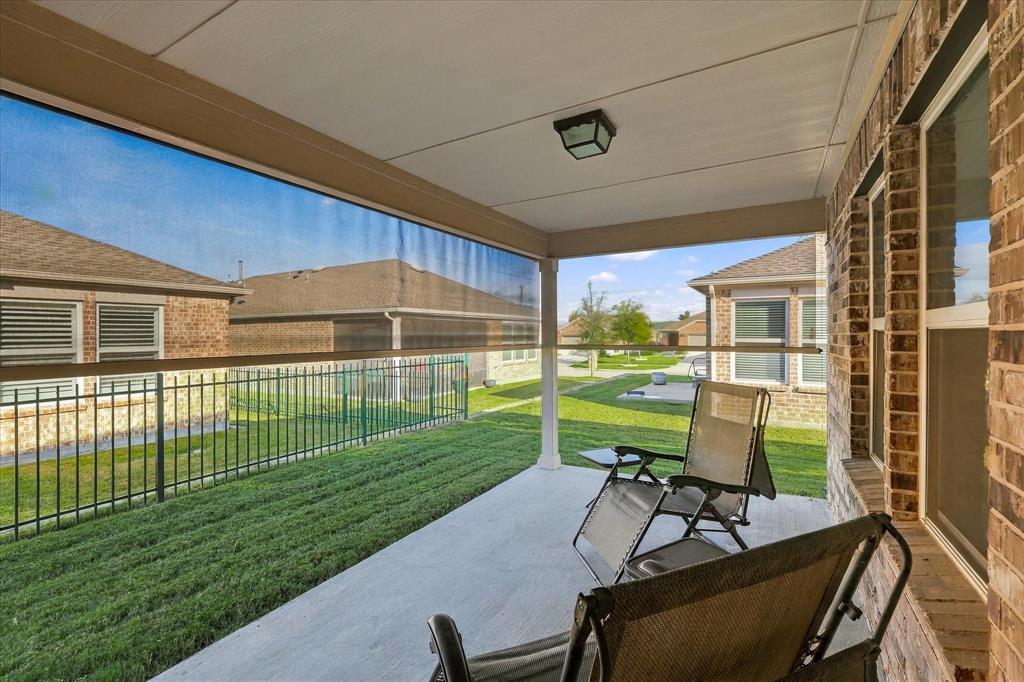 Covered patio featuring concrete flooring, a retractable mesh privacy screen, brick exterior wall, and mounted outdoor lighting