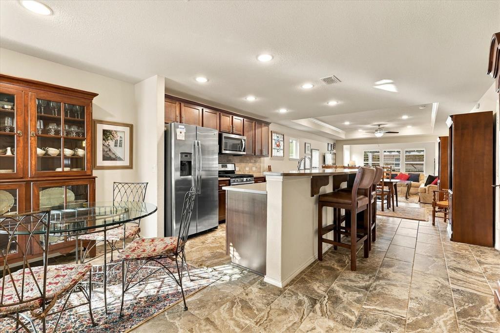 Kitchen featuring stained-wood cabinetry, stainless steel appliances, recessed lighting, and stone-finish tile flooring with an integrated breakfast bar
