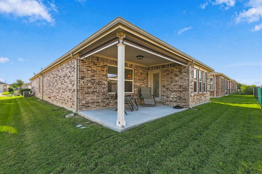 Covered rear concrete patio featuring brick exterior walls, a support column, and a retractable fabric awning