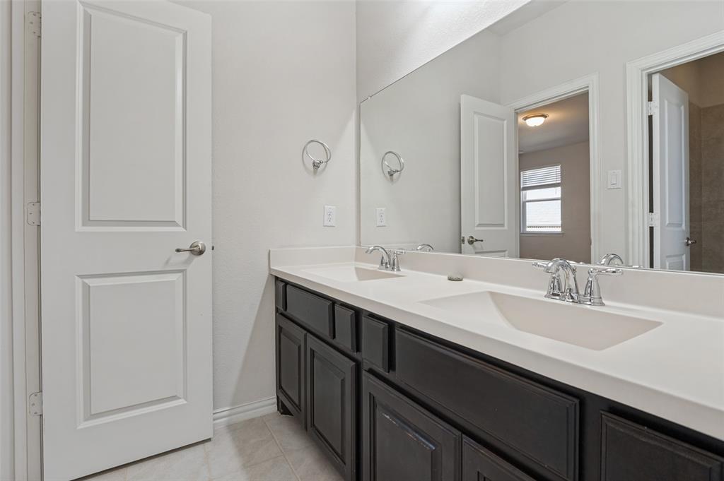Dual-sink vanity with dark cabinetry, integrated solid-surface countertop, chrome hardware, and a wall-to-wall mirror