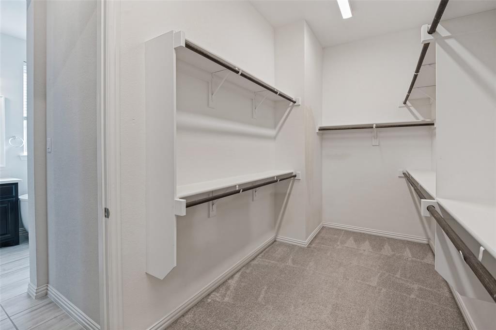 Walk-in closet featuring tiered shelving, integrated hanging rods, neutral carpeting, and overhead lighting