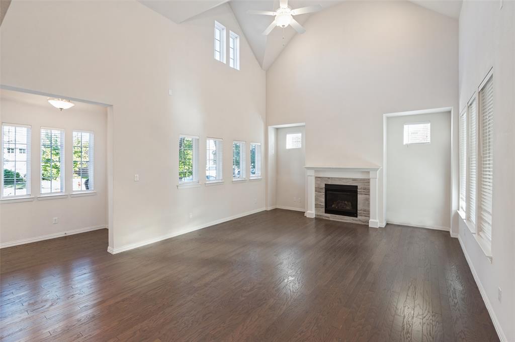 Vaulted ceilings featuring a central ceiling fan, wood-finish flooring, multi-pane windows, and a fireplace with a stone-surround mantel