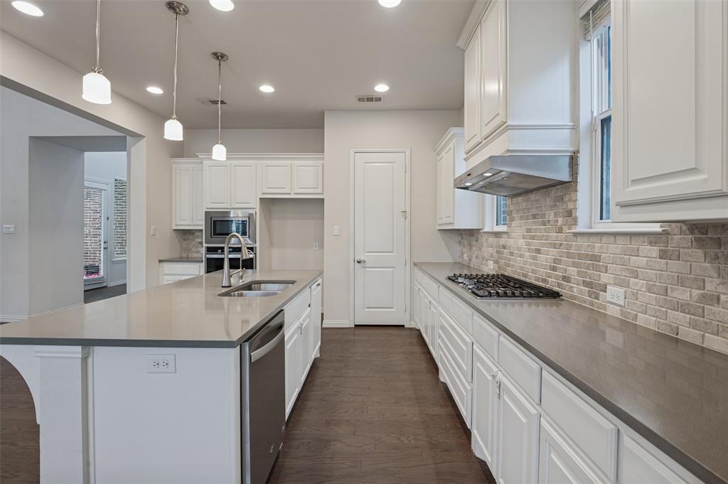 Kitchen featuring white shaker cabinetry, stone-finish countertops, brick-style tile backsplash, stainless steel appliances, and wood-finish flooring