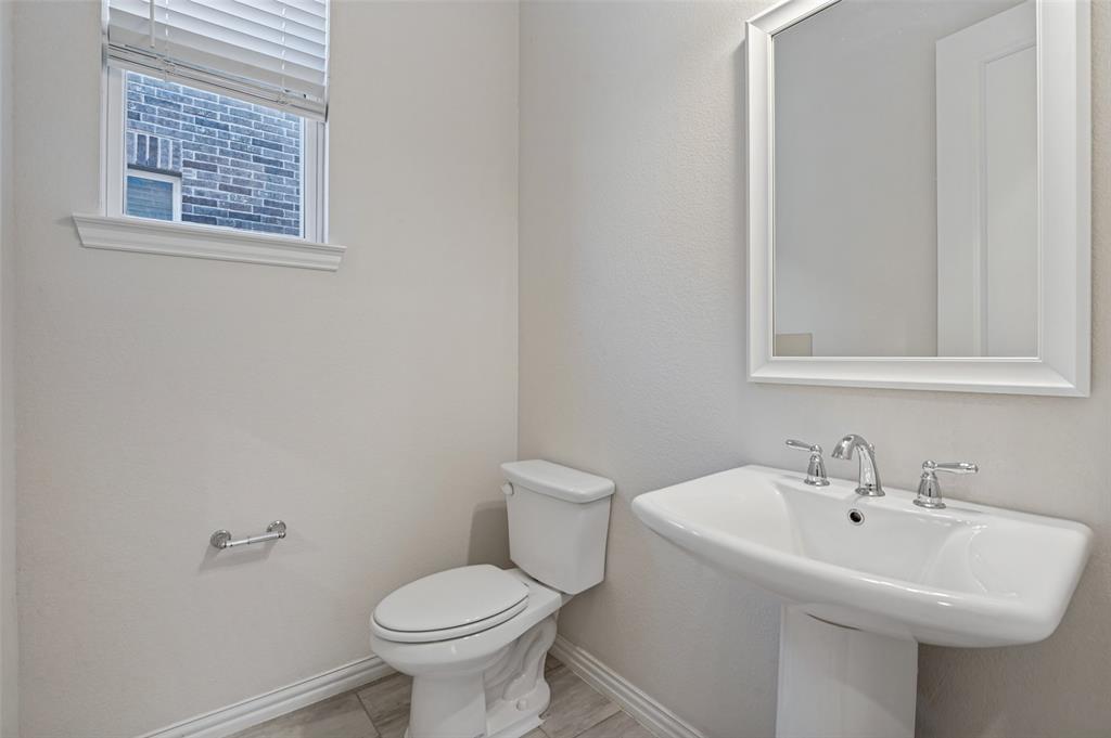 Pedestal sink with polished chrome widespread faucet, white framed mirror, dual-flush toilet, and wood-finish tile flooring Pedestal sink with polished chrome widespread faucet, white framed mirror, dual-flush toilet, and wood-finish tile flooring