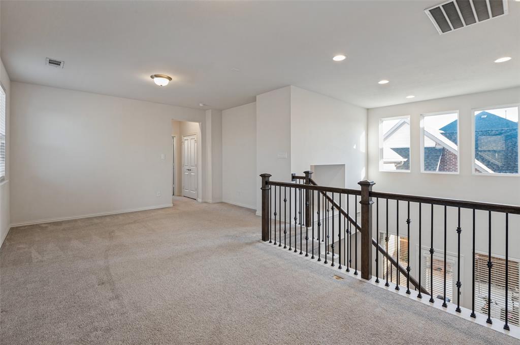 Open loft area featuring neutral wall-to-wall carpeting, recessed lighting, and a metal balustrade with wood-finish railing