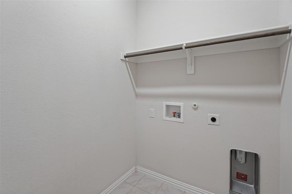 Utility area featuring tile flooring, neutral wall paint, and a built-in shelf with a metal hanging rod Utility area featuring tile flooring, neutral wall paint, and a built-in shelf with a metal hanging rod