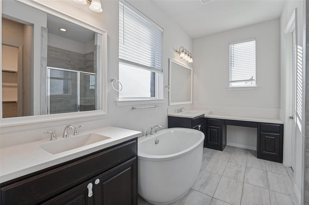 Bathroom featuring a freestanding oval soaking tub, dual dark-finish cabinetry with light countertops, rectangular undermount sinks, and light-tone tile flooring Bathroom featuring a freestanding oval soaking tub, dual dark-finish cabinetry with light countertops, rectangular undermount sinks, and light-tone tile flooring