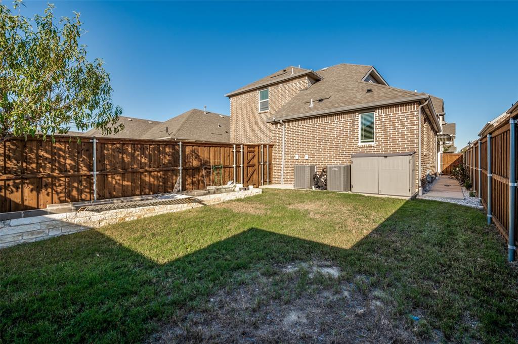Private backyard featuring a brick exterior, stone-accented retaining wall, wood privacy fencing, and a concrete side pathway