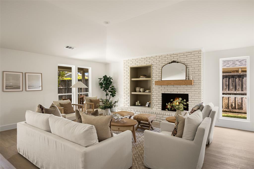Bright and inviting living area featuring vaulted ceilings, a beautifully updated brick fireplace with wood mantel, built-in shelving, and large windows overlooking the backyard.