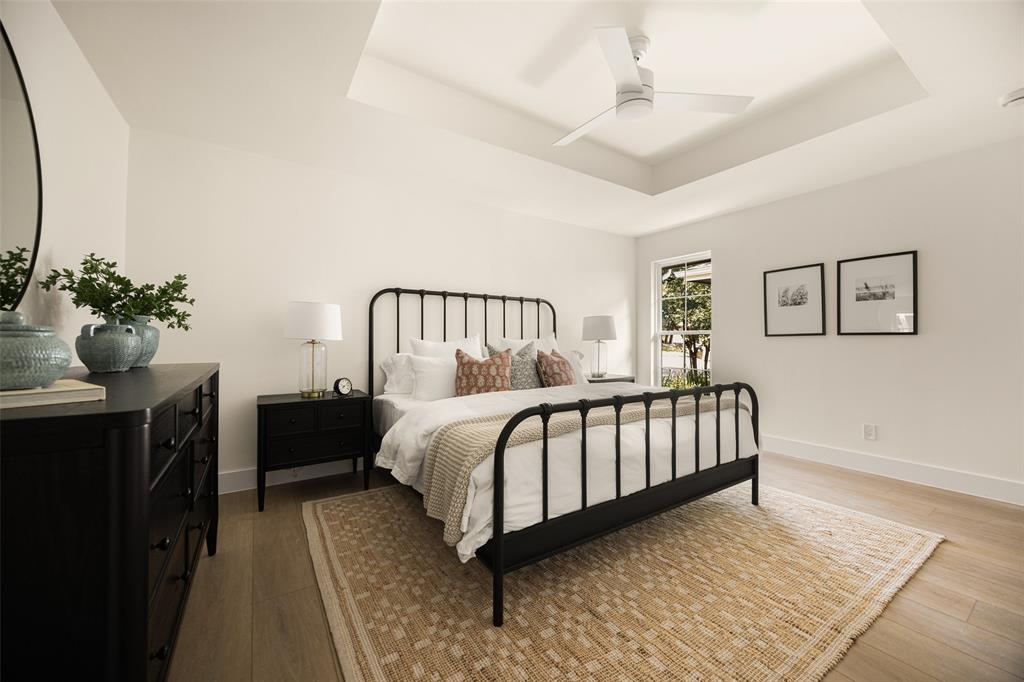 Beautifully updated primary bedroom featuring a tray ceiling, modern ceiling fan, warm wood-like flooring, and abundant natural light that creates a bright, inviting atmosphere