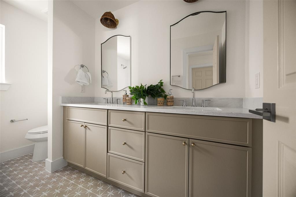 Fully updated secondary bathroom featuring a double vanity, refined finishes, decorative tile flooring, and a bright tub-shower surround with clean, timeless tilework.