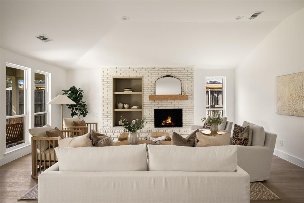 Bright and inviting living area featuring vaulted ceilings, a beautifully updated brick fireplace with wood mantel, built-in shelving, and large windows overlooking the backyard.