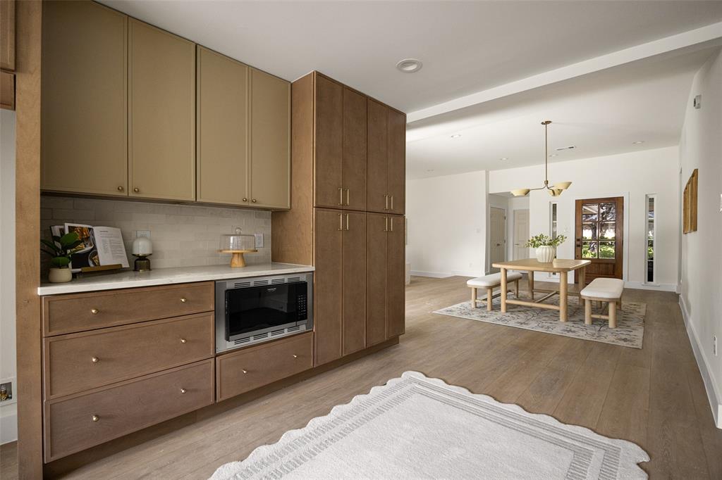 Sophisticated, designer-inspired kitchen featuring rich wood cabinetry, elegant stone-look countertops, artisan-style tile backsplash, warm brass accents, stainless steel appliances, and abundant natural light.