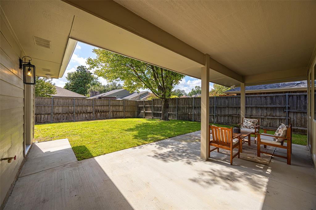 Covered patio with generous space for outdoor seating and dining, overlooking the fenced backyard and mature shade tree.