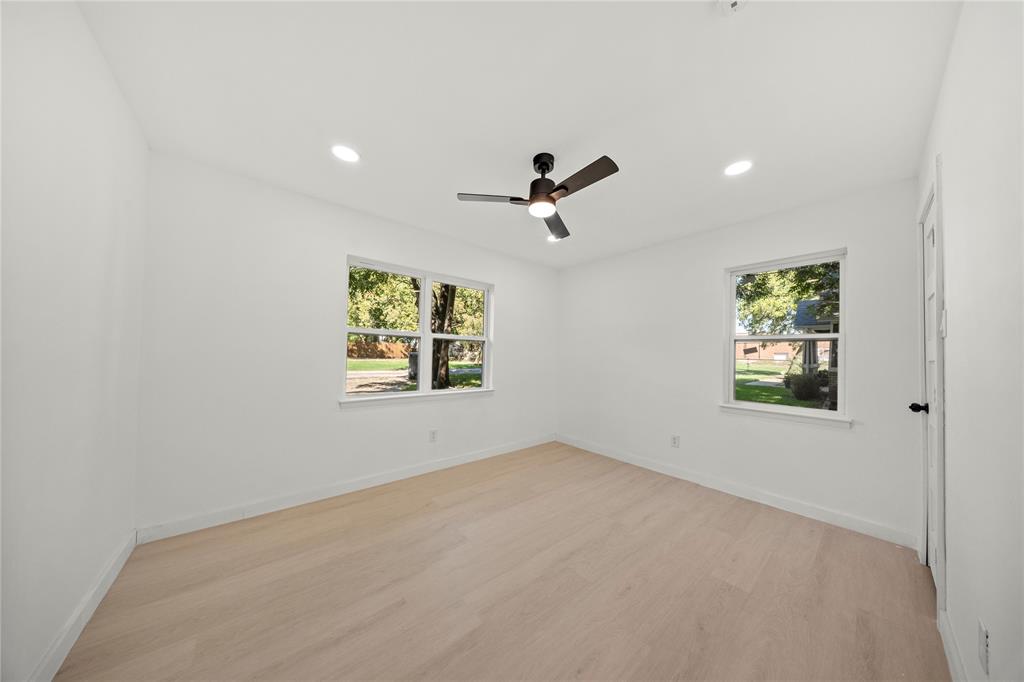 Neutral-toned interior space featuring light wood-finish flooring, recessed lighting, dual windows, and a matte black ceiling fan