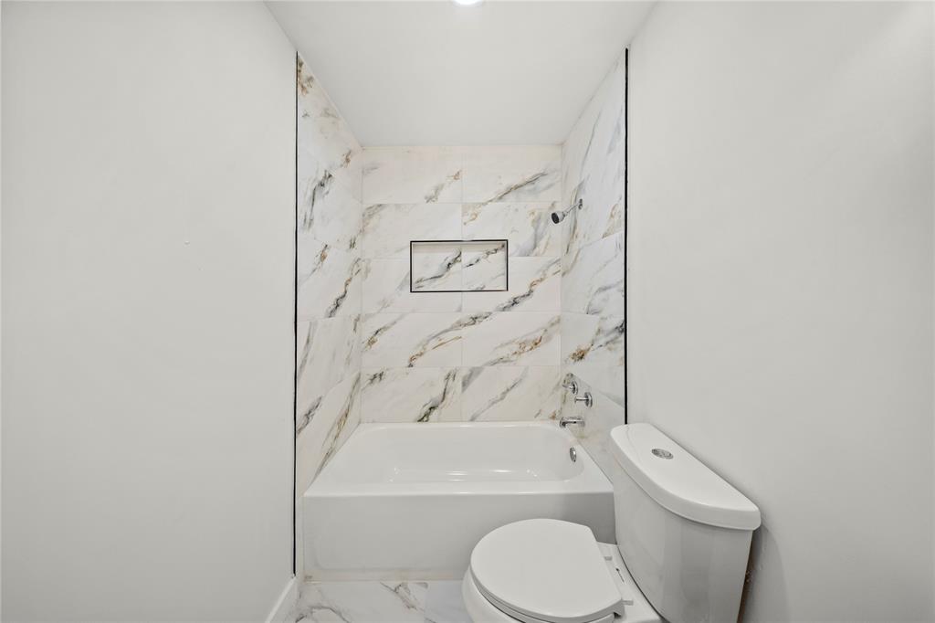 Full-height wall surround with stone-finish porcelain tile, integrated recessed shelving, and a white soaking tub featuring polished chrome plumbing fixtures