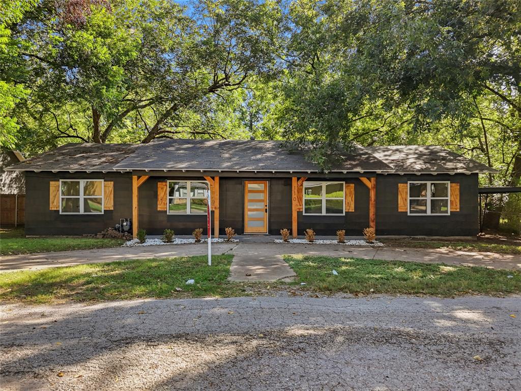 Exterior facade featuring dark-toned horizontal siding, wood-finish window shutters, exposed timber support beams, and a modern glass-paneled entry door