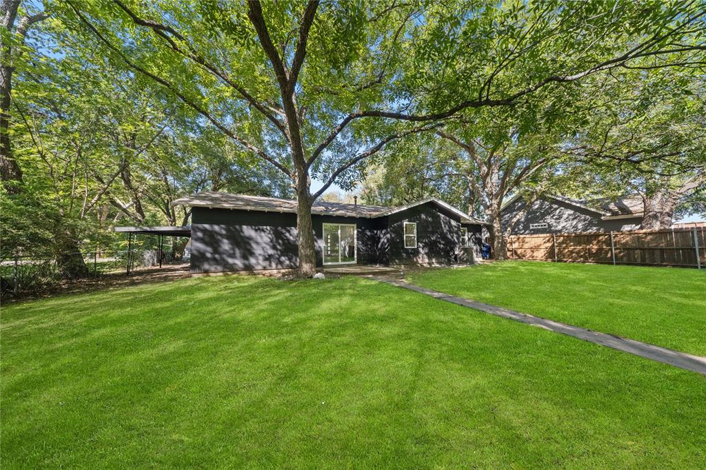 Expansive backyard featuring a large lawn, mature trees, a paved walkway, and a wooden privacy fence