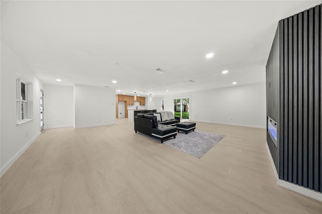 Open-concept interior featuring wood-finish flooring, recessed lighting, and a floor-to-ceiling vertical slat accent wall with an integrated electric fireplace
