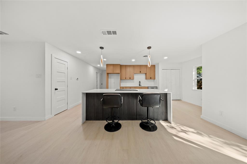 Kitchen featuring light wood-finish cabinetry, a central island with a ribbed facade, integrated cooktop, recessed lighting, and wood-finish flooring