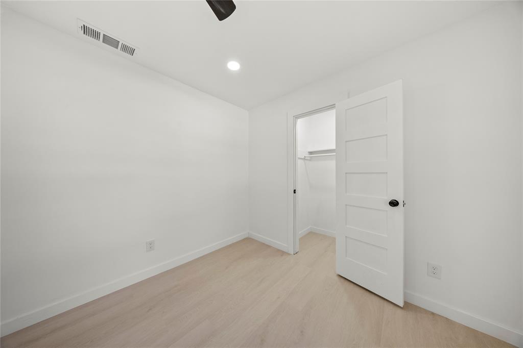 Room featuring wood-finish flooring, recessed lighting, and a five-panel interior door with matte black hardware, providing entry to a walk-in closet with built-in shelving