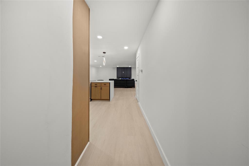 Light-toned wood-finish flooring, recessed ceiling lighting, and kitchen cabinetry featuring a stone-style countertop and dark hardware