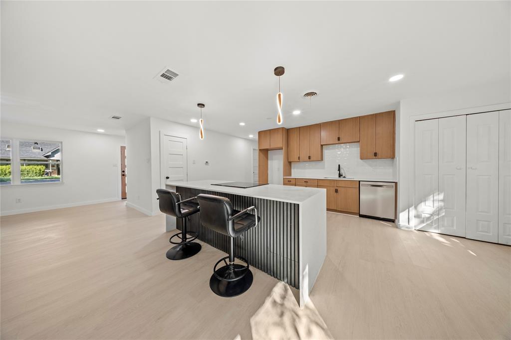 Kitchen featuring a center island with a stone-finish countertop and vertical slat detail, flat-panel wood-finish cabinetry, white subway tile backsplash, stainless steel dishwasher, and minimalist pendant lighting