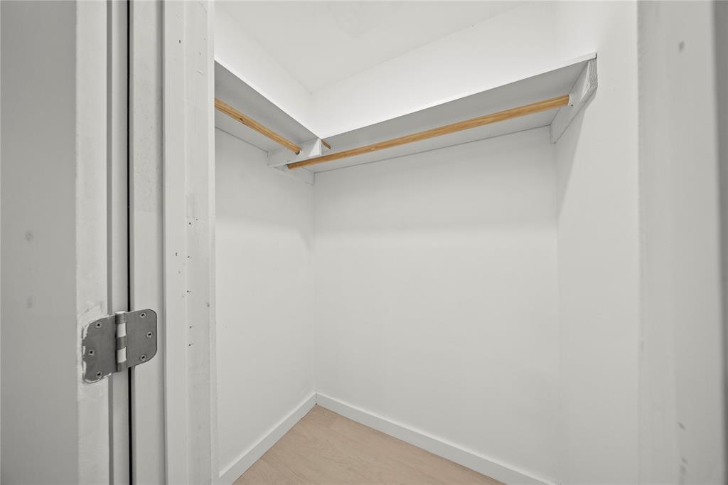 Walk-in closet featuring white walls, wood-finish flooring, and integrated wrap-around shelving with wood hanging rods