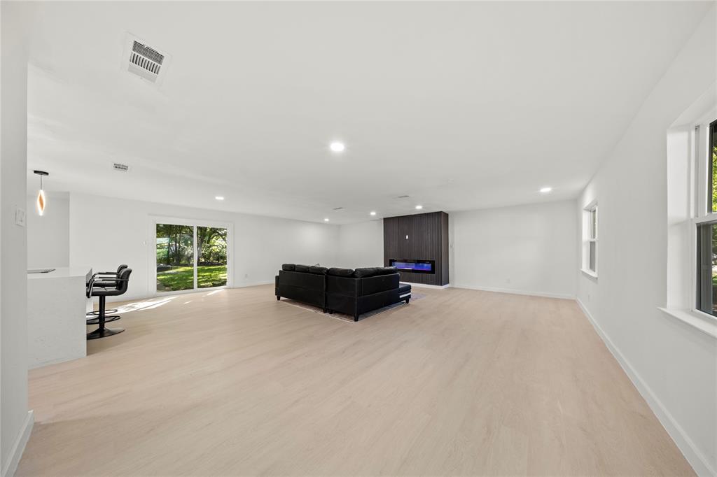 Open-concept interior featuring wood-finish flooring, recessed lighting, a modern floor-to-ceiling fireplace surround with integrated electric insert, and sliding glass doors