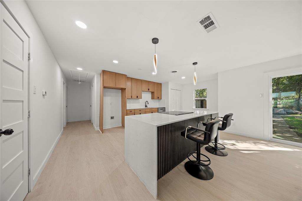 Kitchen featuring wood-finish cabinetry, a waterfall-edge island with a vertical-slat base, neutral solid-surface countertops, recessed lighting, and wood-finish flooring