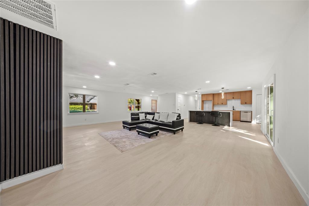 Open floor plan featuring light wood-finish flooring, a vertical-slat accent wall, recessed lighting, and a kitchen island with built-in cabinetry