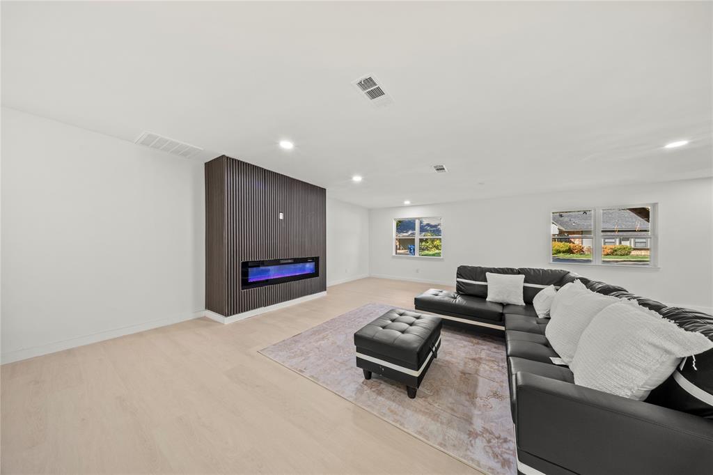 Living space featuring light wood-finish flooring, recessed lighting, and a floor-to-ceiling dark wood-slatted feature wall with an integrated linear electric fireplace