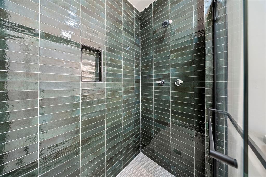 Walk-in shower featuring glossy, forest-green elongated subway tile, a recessed wall niche, chrome rainfall showerhead, chrome wall-mounted fixtures, and a glass-enclosed door