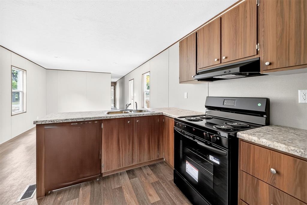 Kitchen featuring wood-finish cabinetry, light-toned countertops, a black range, and a built-in sink