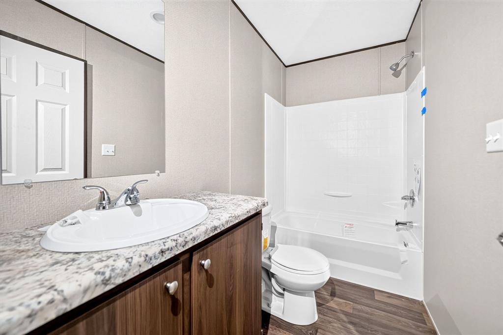 Wood-finish flooring, vanity with laminate countertop, integrated sink, and chrome fixtures