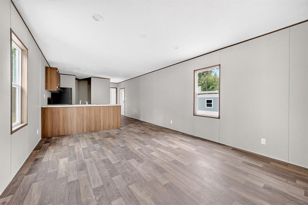 Wood-finish flooring throughout, recessed ceiling lighting, a kitchen bar with wood-finish paneling, and an integrated kitchen with dark cabinetry and appliances