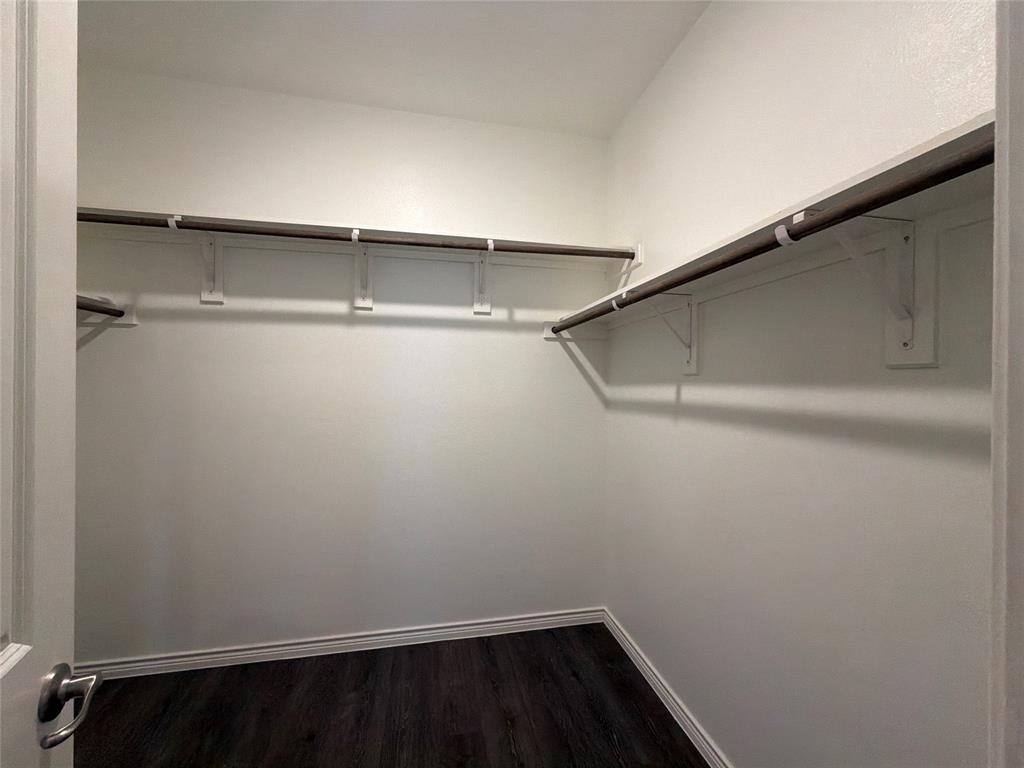 Storage closet featuring dark wood-finish flooring and dual-level shelving with integrated clothing rods